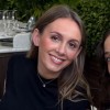 Smiling woman with light brown hair, outdoors with greenery in the background.