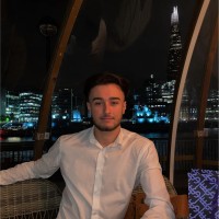 Man in a white shirt seated in a restaurant with city lights in the background.